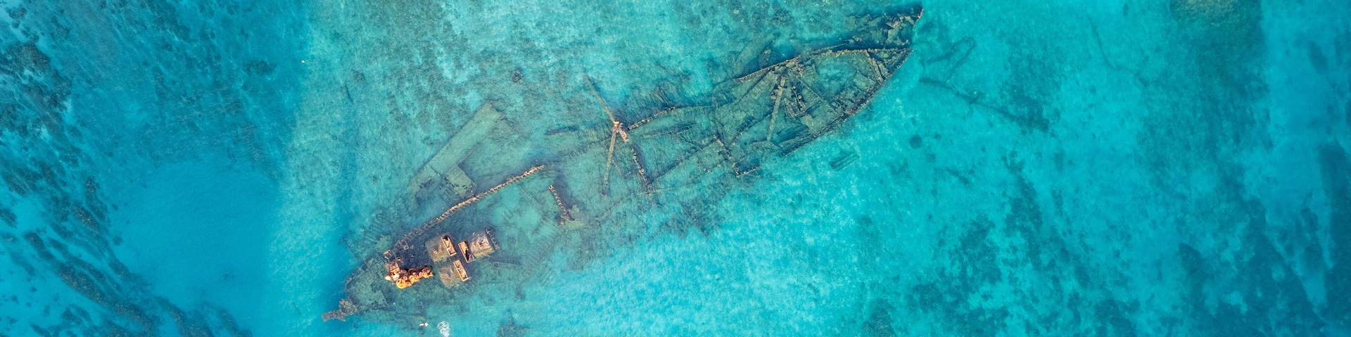 An aerial view of a sunken shipwreck with coral growth and clear turquoise waters.