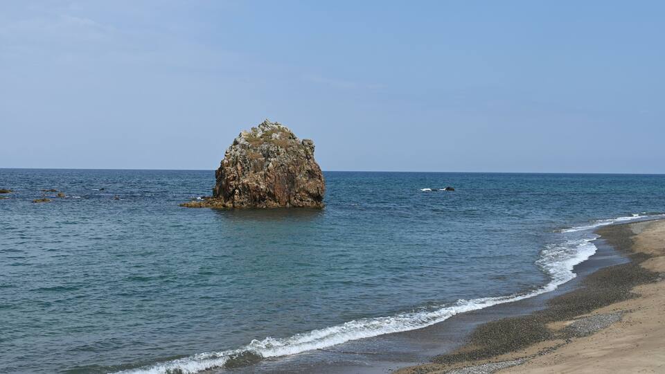 A rocky outcrop in the sea with a sandy beach in the foreground.