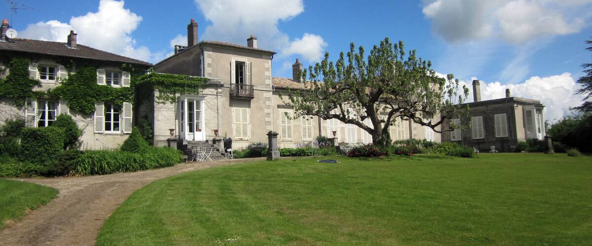A large estate with a well-maintained lawn, a prominent tree, and classic architecture.