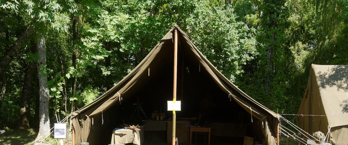 A tent set up in a forest with trees and a table with items on it.