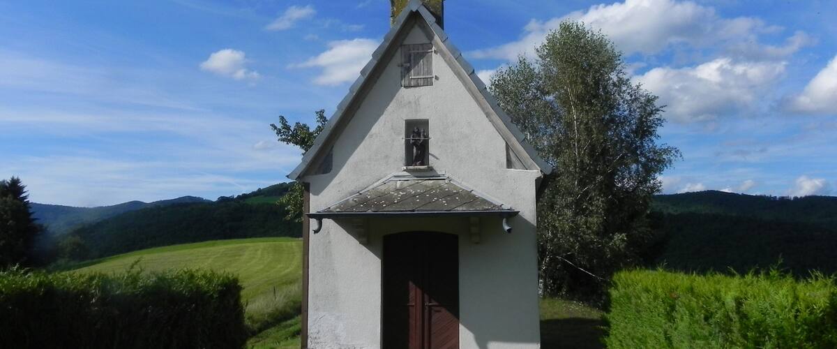 A small white church with a cross on top, surrounded by green fields and hills.