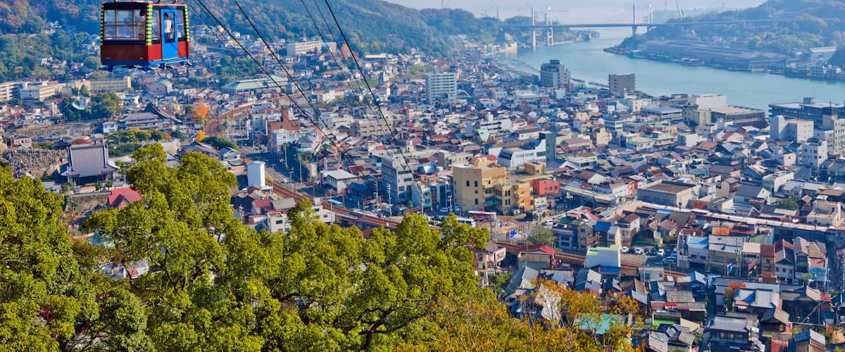 A cable car over a densely populated city with a river and a bridge in the background.