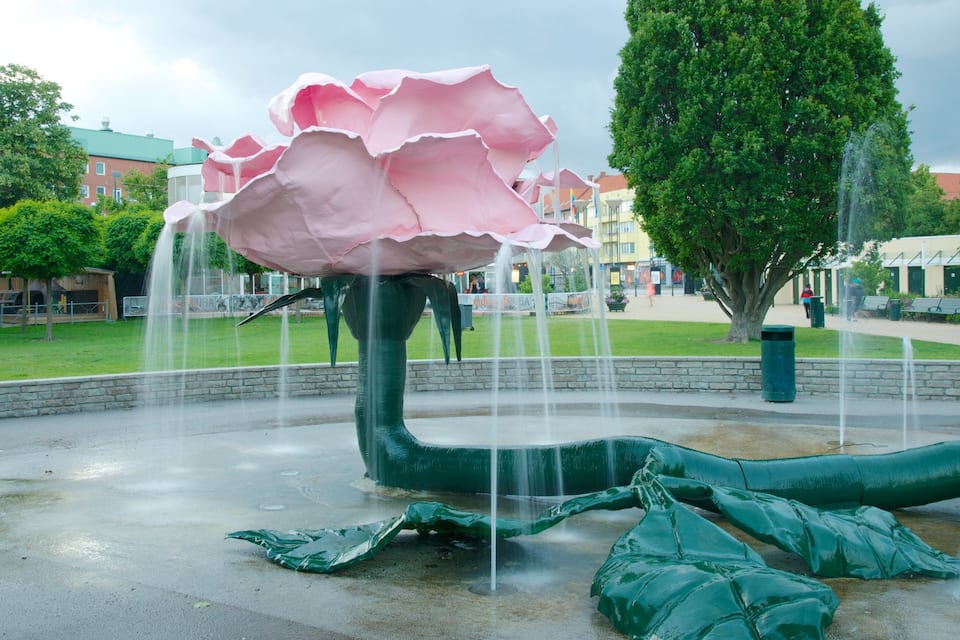 Een grote, roze waterfontein in de vorm van een bloem, met meerdere waterstralen in een park.