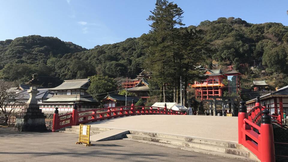 A traditional Japanese temple complex with red and white buildings, surrounded by lush greenery and hills.