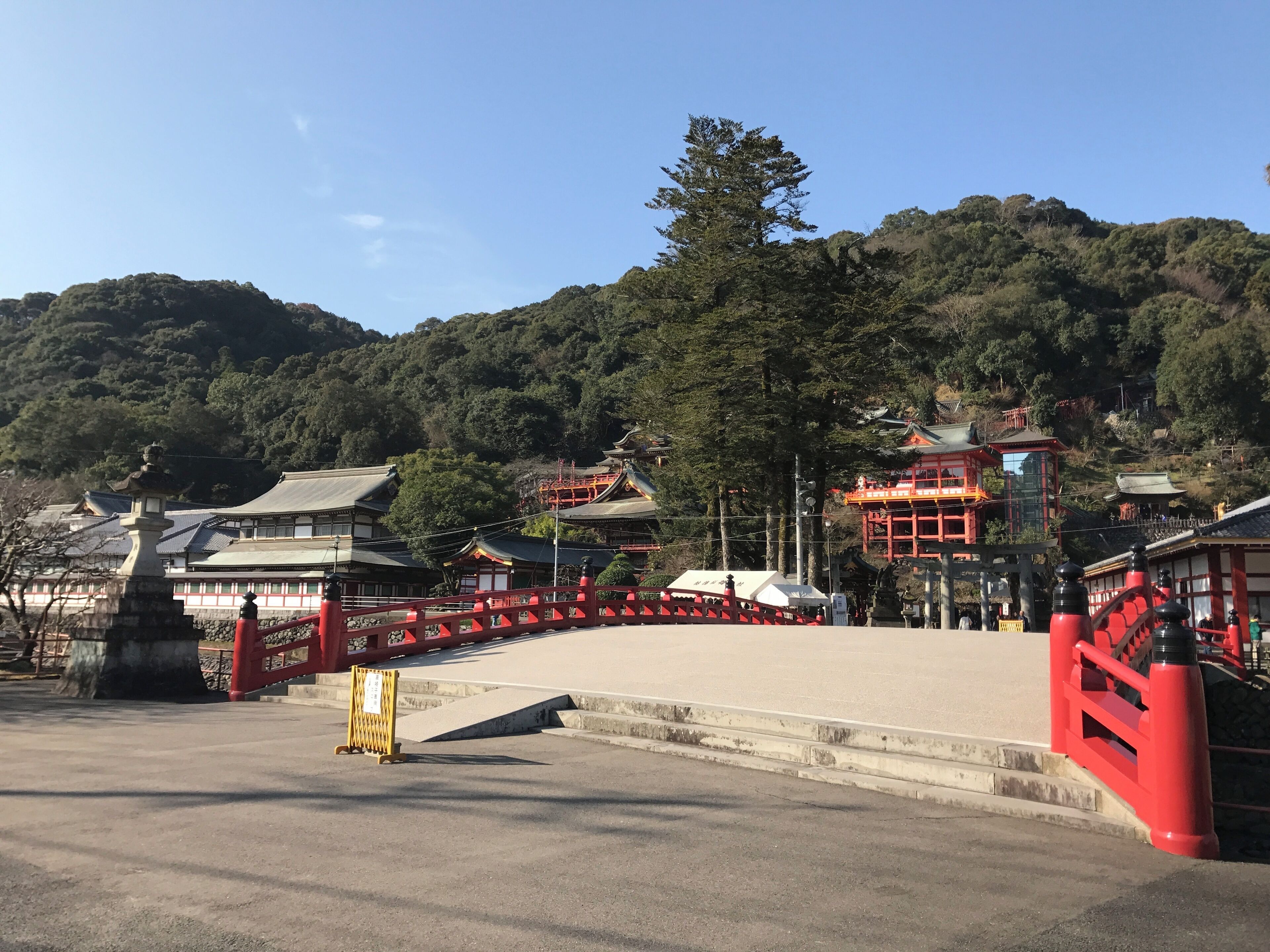 A traditional Japanese temple complex with red and white buildings, surrounded by lush greenery and hills.
