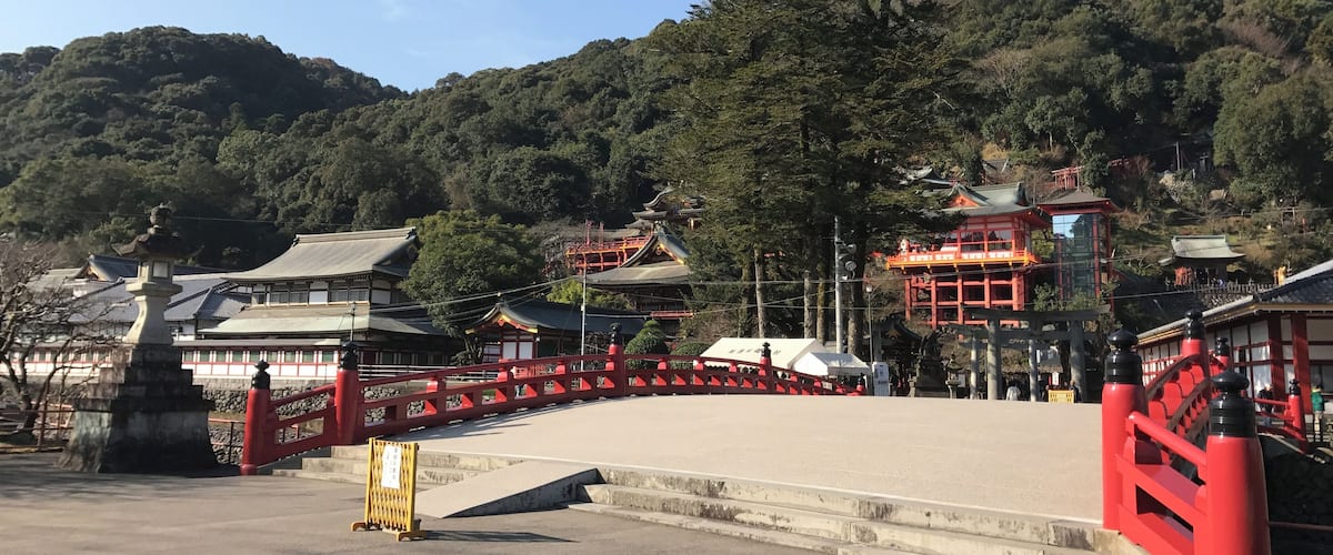 A traditional Japanese temple complex with red and white buildings, surrounded by lush greenery and hills.