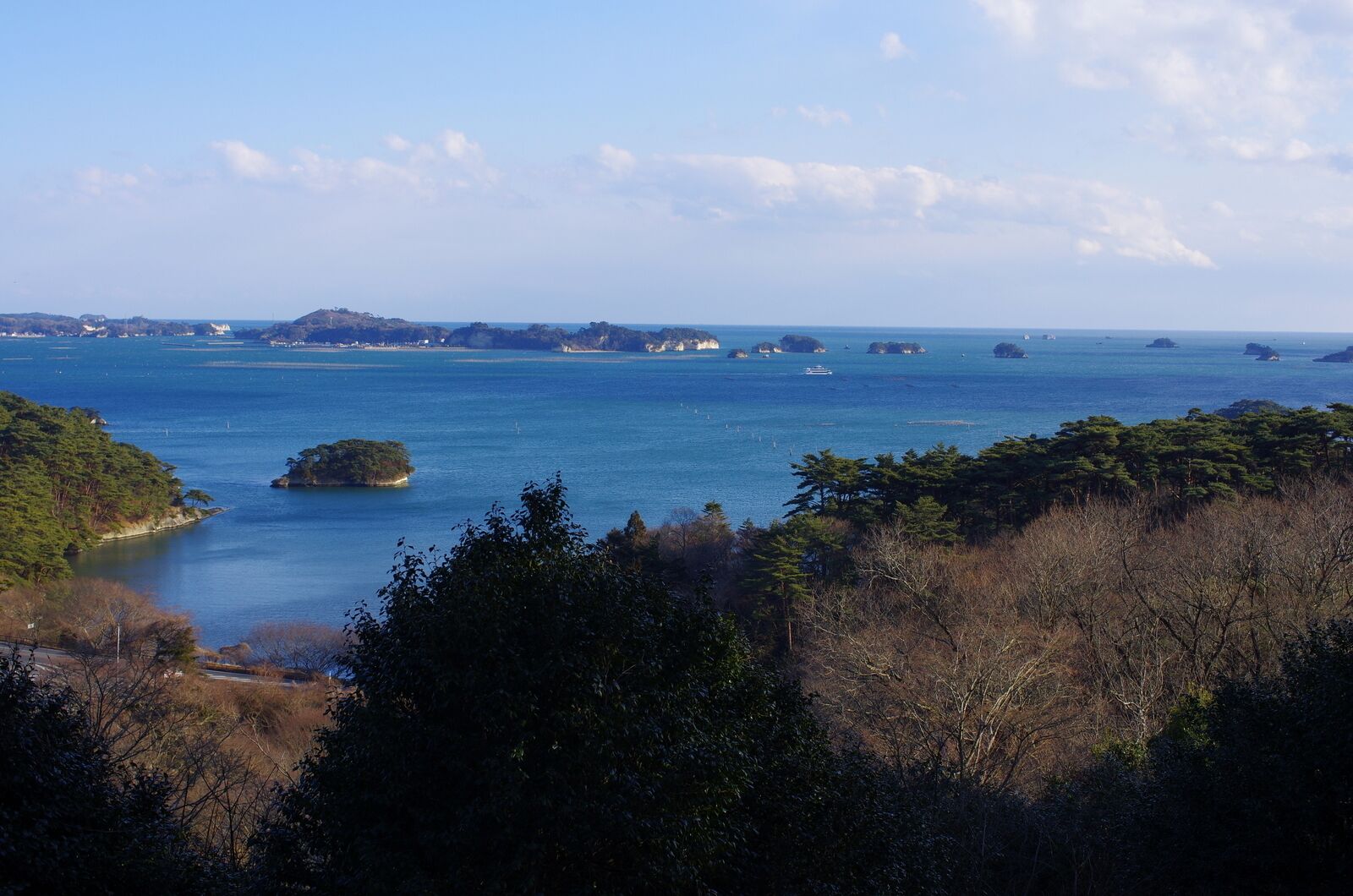A coastal landscape with a clear blue sea, several small islands, and dense forested areas.