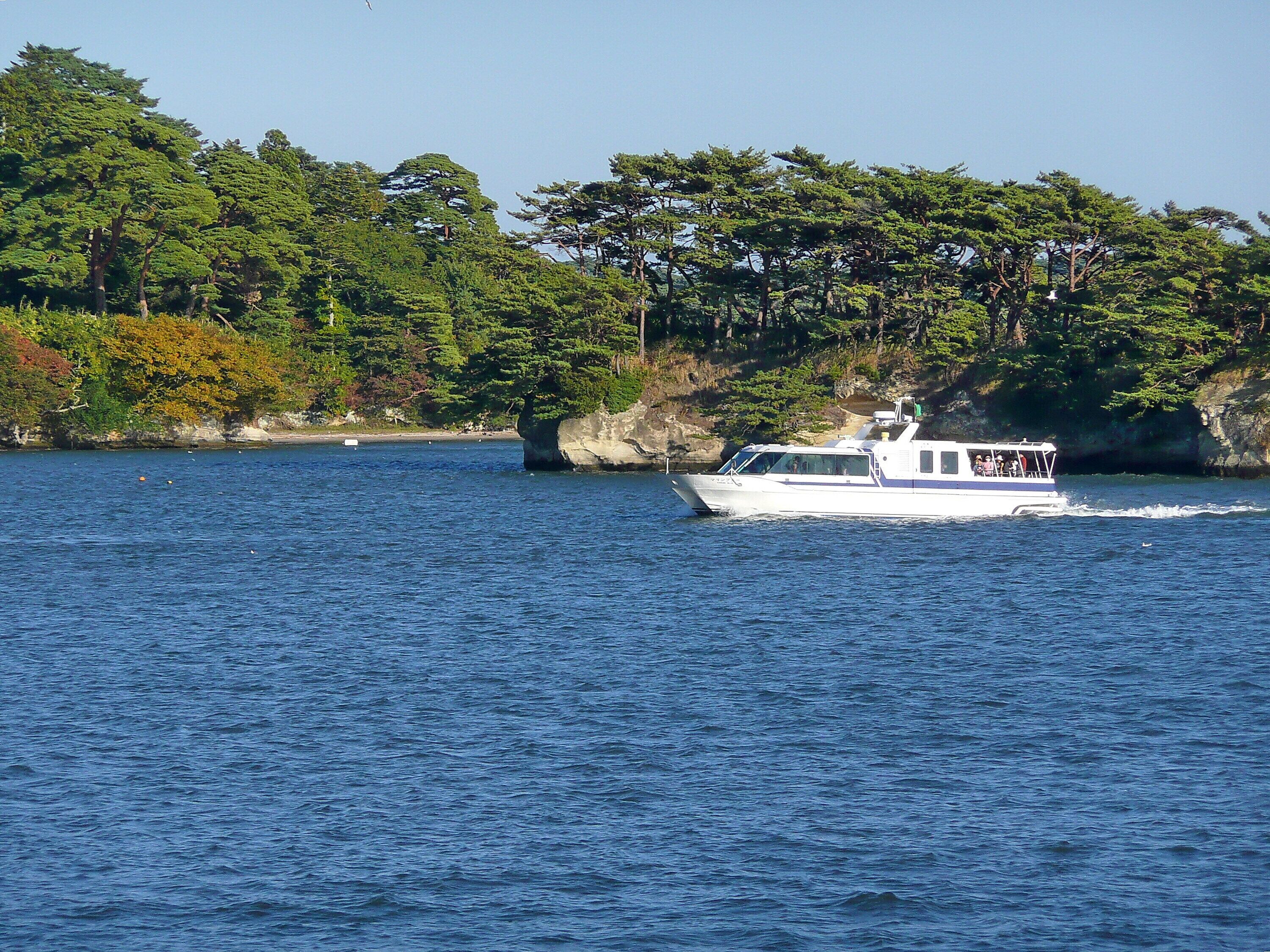 A white boat on a calm body of water with a rocky shoreline and dense green foliage in the background.