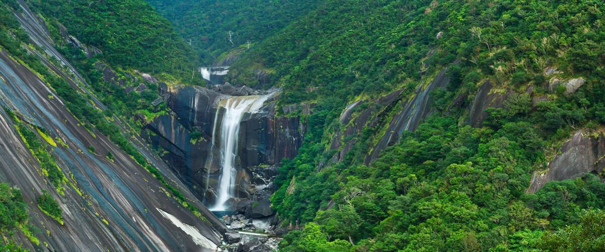 A large waterfall cascading down a steep, rocky gorge surrounded by dense green forest.