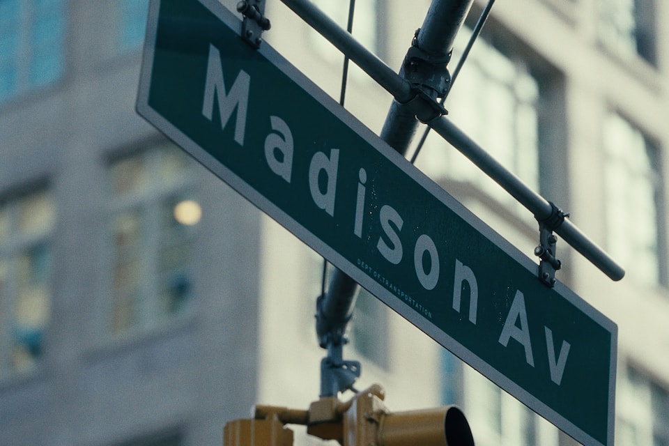 A street sign for 'Madison Ave' with a blurred building in the background.