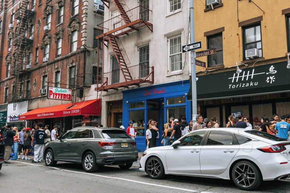 A busy street with cars, pedestrians, and various storefronts including a pizzeria and a restaurant.