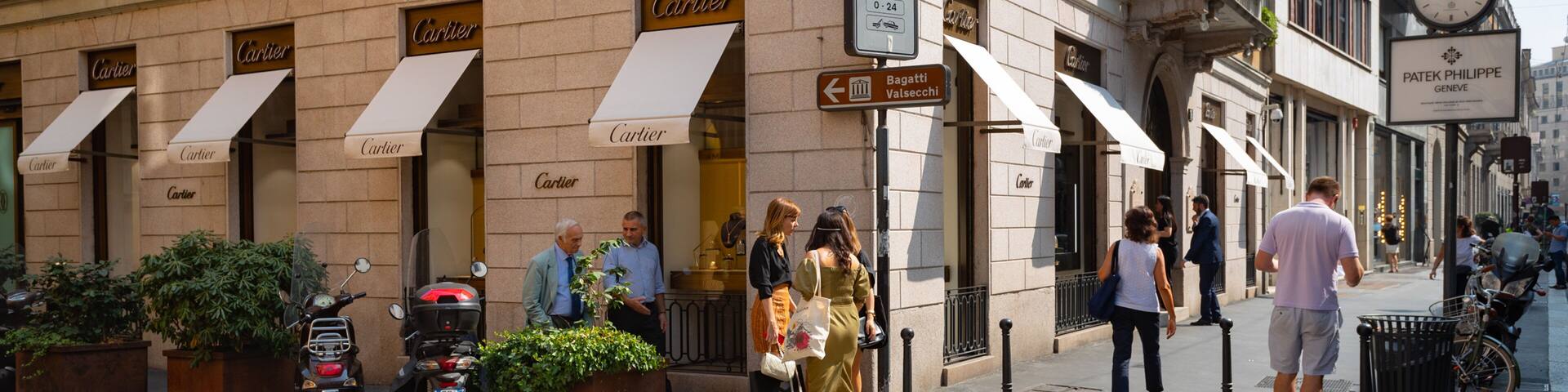 A street with pedestrians, a crosswalk, and storefronts with the name "Cartier".