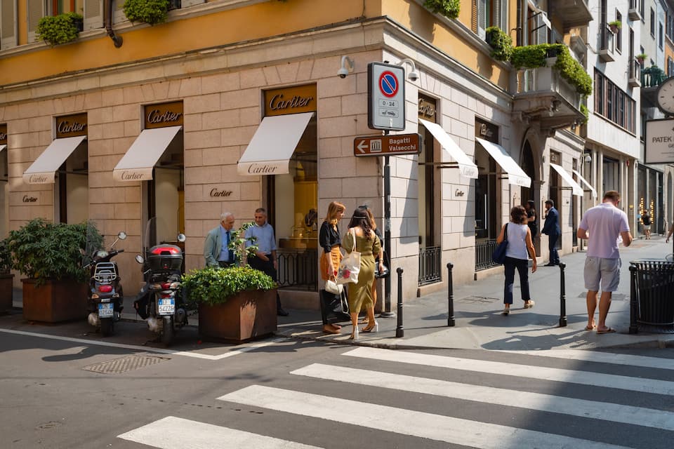 A street with pedestrians, a crosswalk, and storefronts with the name "Cartier".