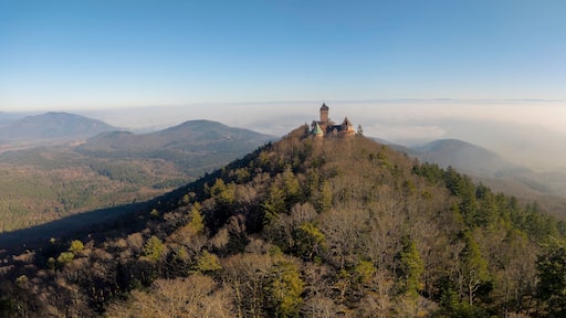 Una montaña con un castillo en la cima, rodeada de colinas boscosas y un cielo despejado.