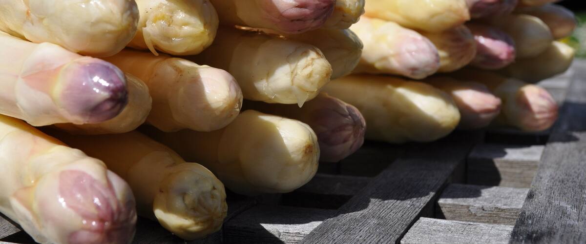 A stack of fresh garlic bulbs with purple tips, placed on a wooden surface.