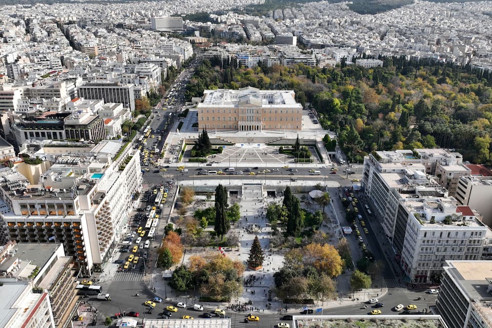 Un paisaje urbano con un edificio gubernamental destacado rodeado de árboles y un cruce de calles con taxis amarillos.