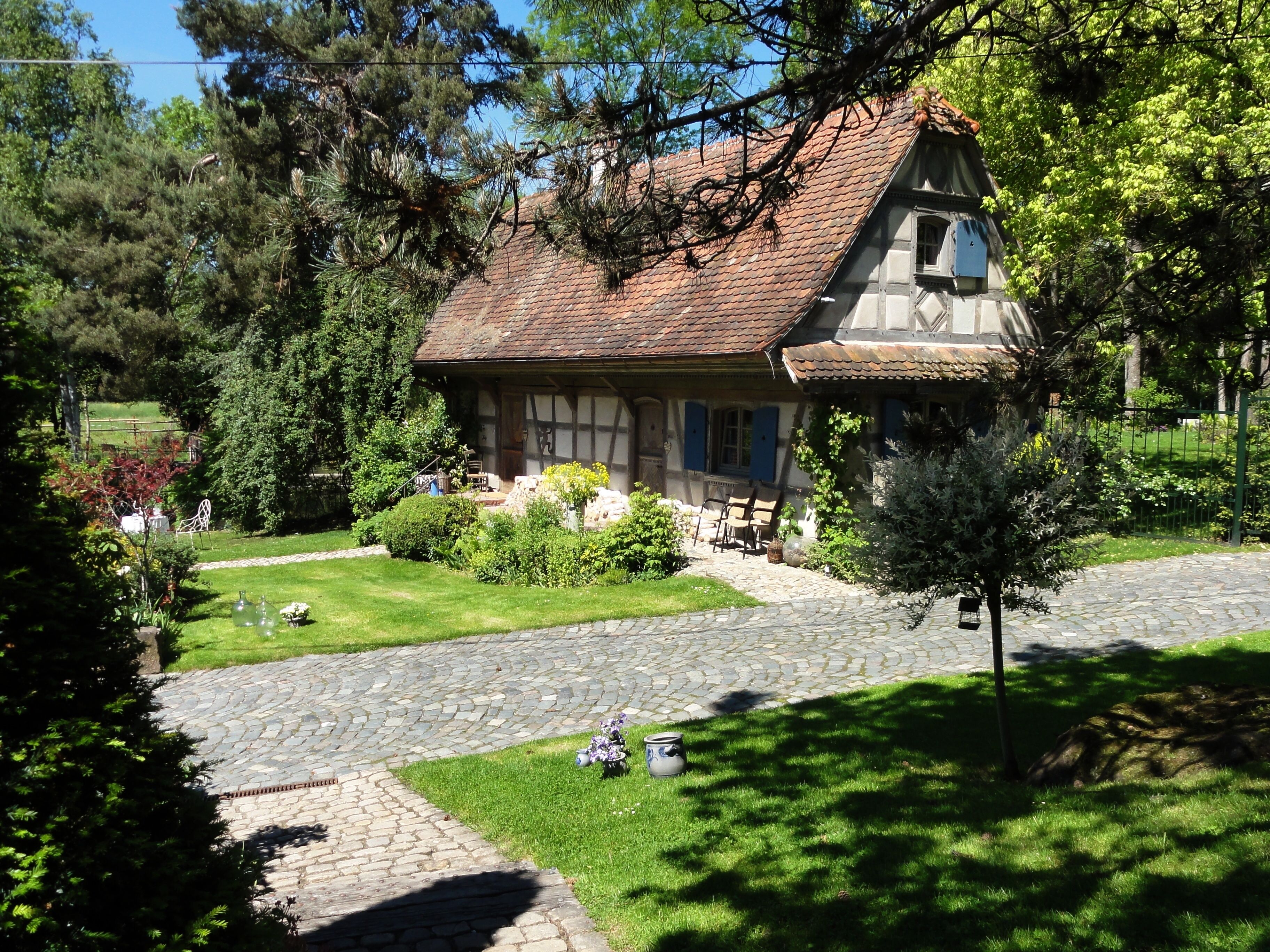 A traditional half-timbered house with a sloped roof, surrounded by a well-maintained garden and a cobblestone pathway.