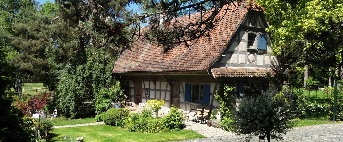 A traditional half-timbered house with a sloped roof, surrounded by a well-maintained garden and a cobblestone pathway.