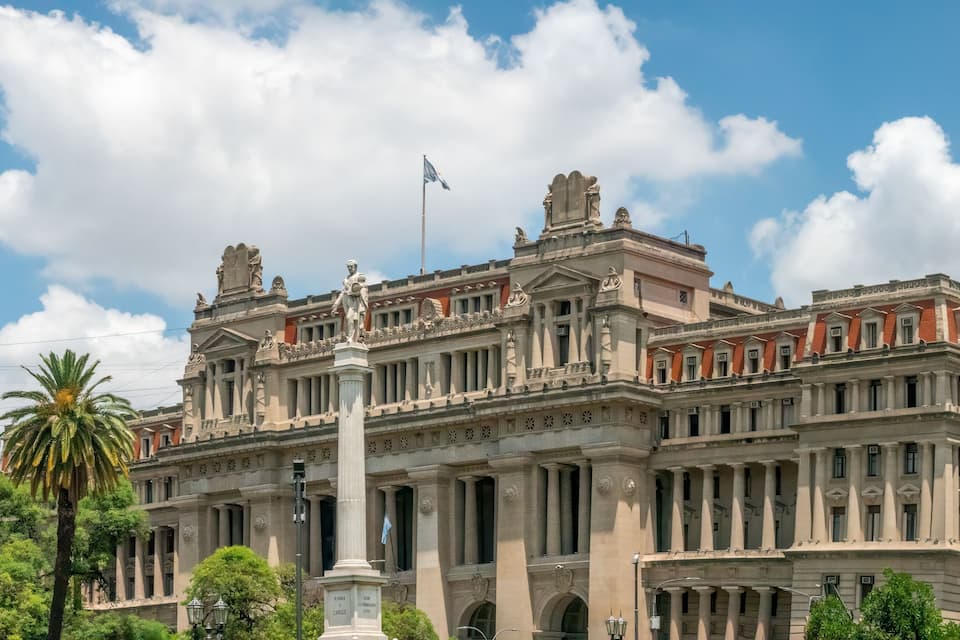 Un edifici gran i ornamentat d'arquitectura clàssica, amb columnes i estàtues, sota un cel amb núvols dispersos.