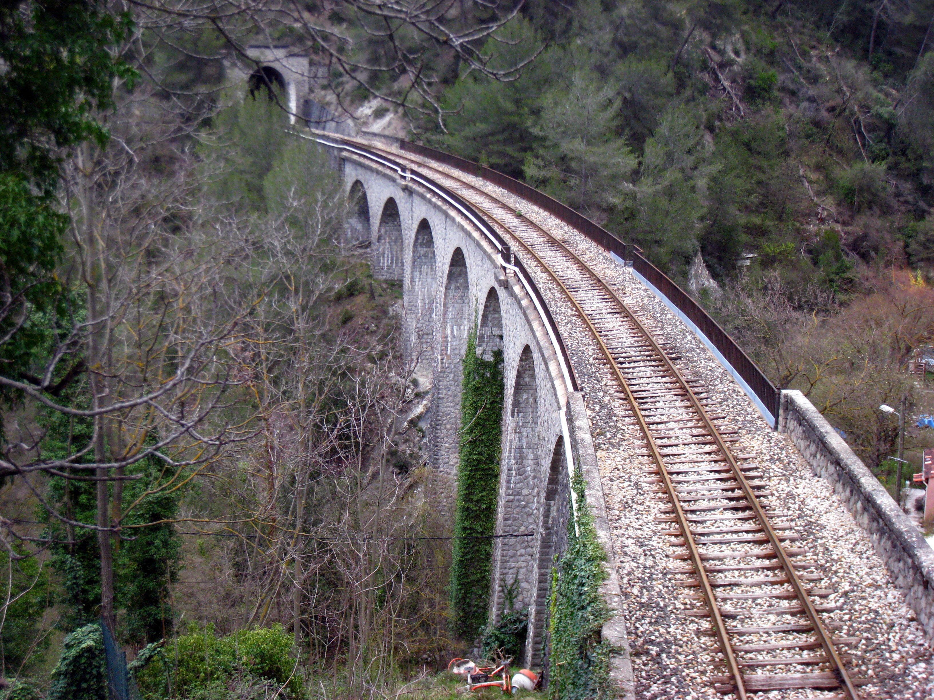 A railway track curving over a stone viaduct surrounded by trees.