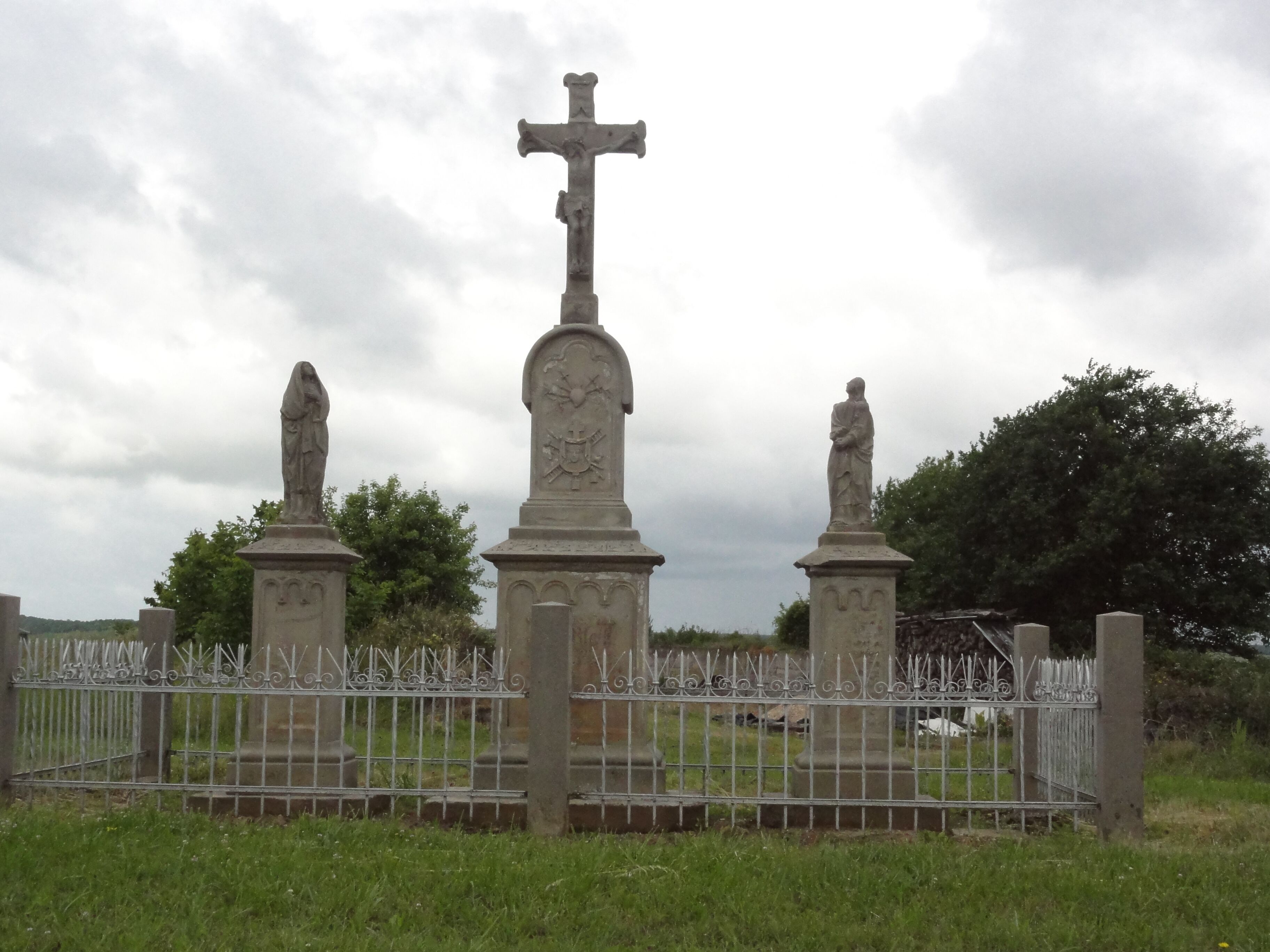 A cemetery with a cross monument, statues, and a metal fence.