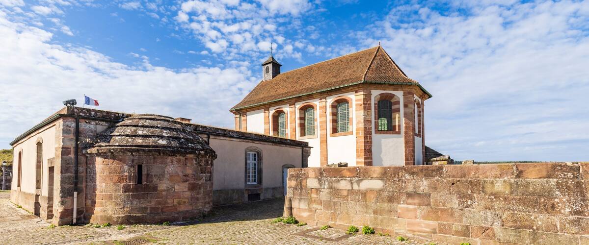 A historic stone building with a bell tower and arched windows, surrounded by a cobblestone courtyard.