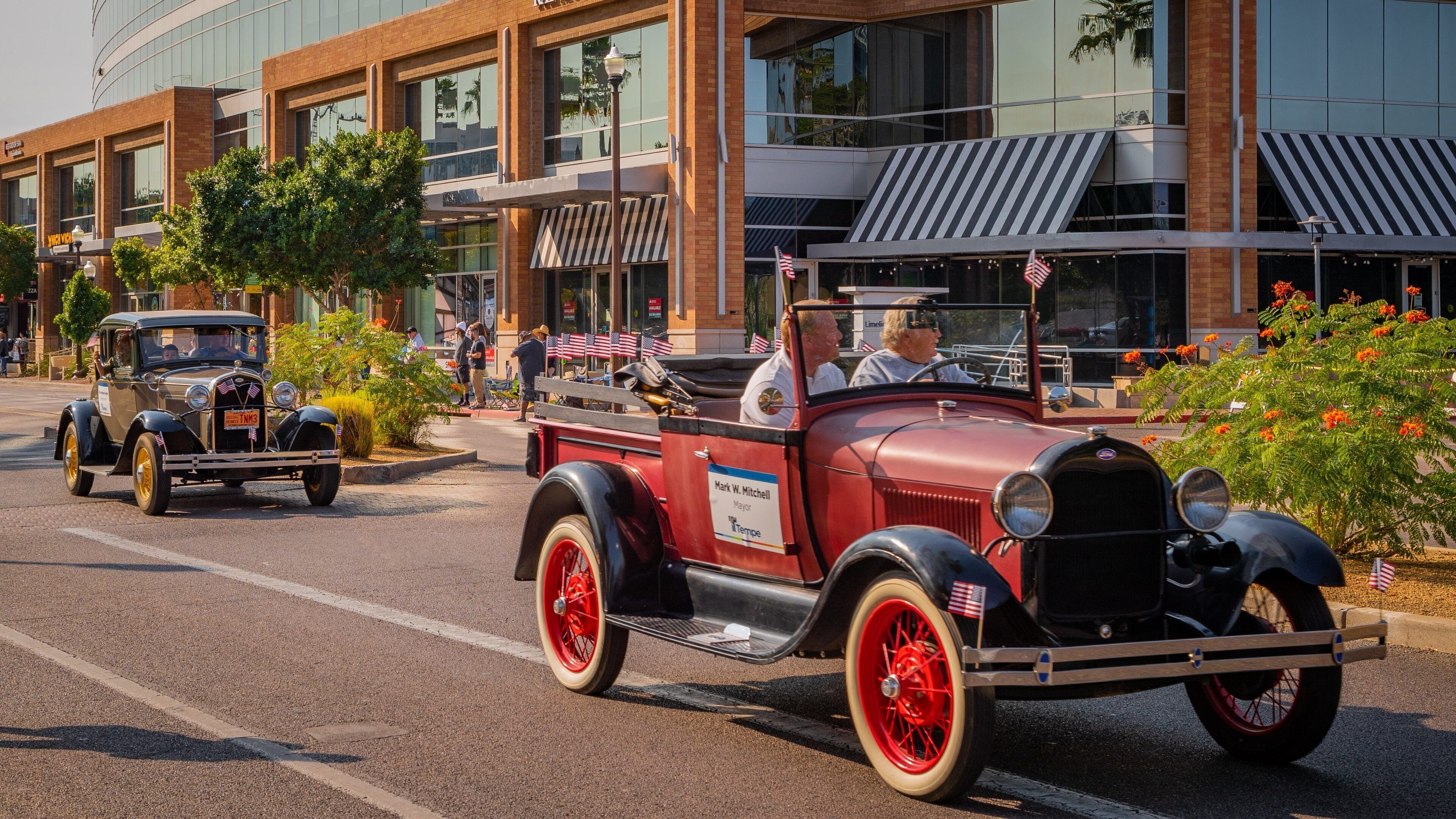 Un desfile de coches antiguos en una calle de la ciudad con edificios modernos al fondo.