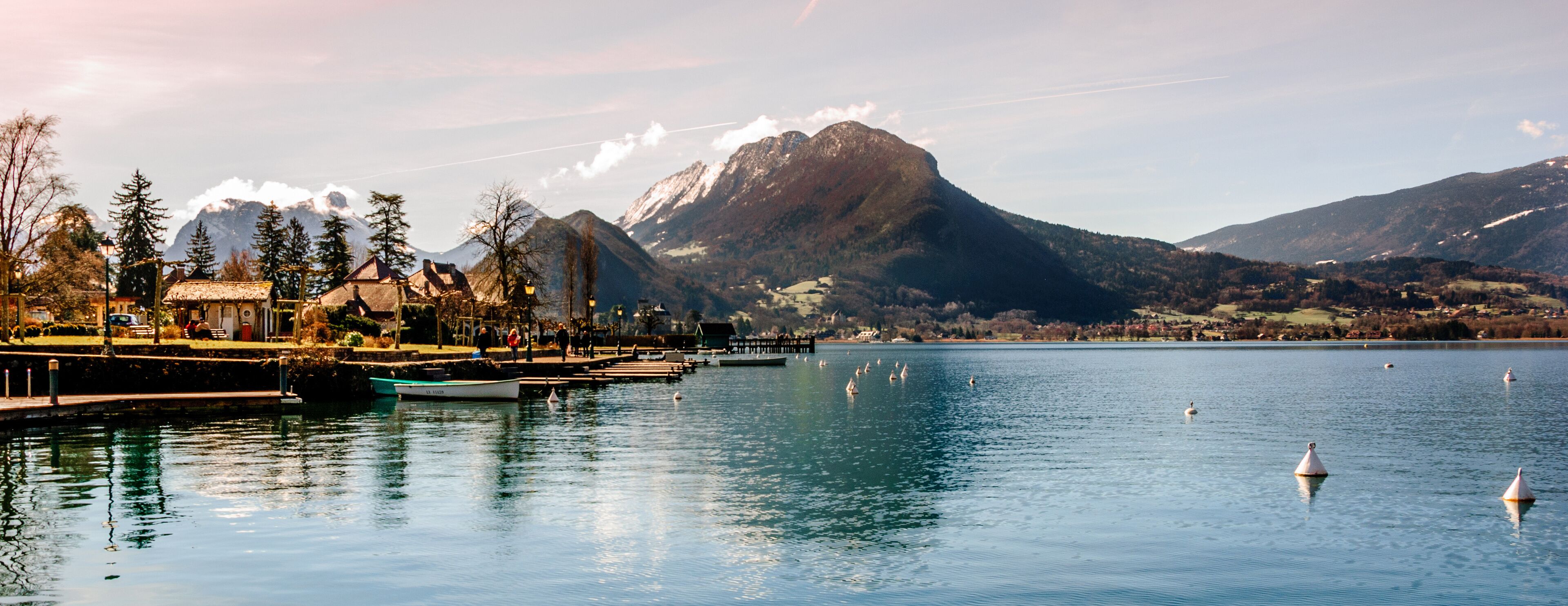 A lake with swans, a boat, a pier, and mountains in the background.