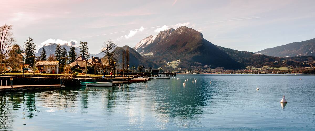 A lake with swans, a boat, a pier, and mountains in the background.