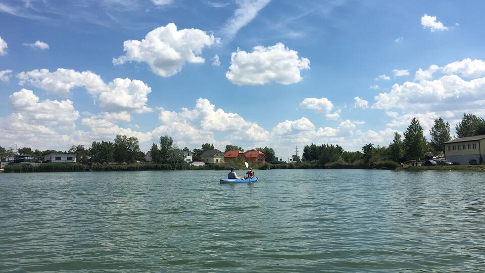 A calm lake with a kayaker in the foreground and houses in the background.