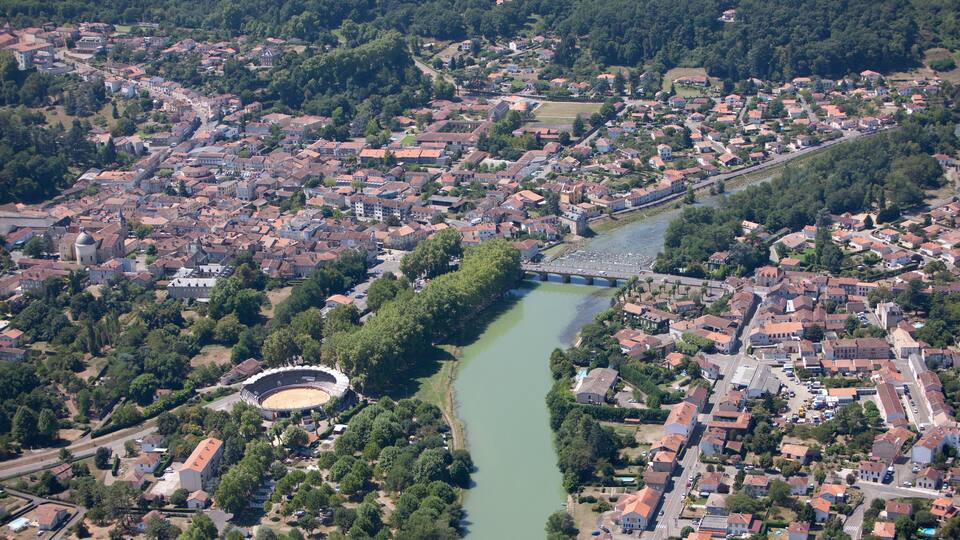 An aerial view of a town with a river, a stadium, and surrounding greenery.
