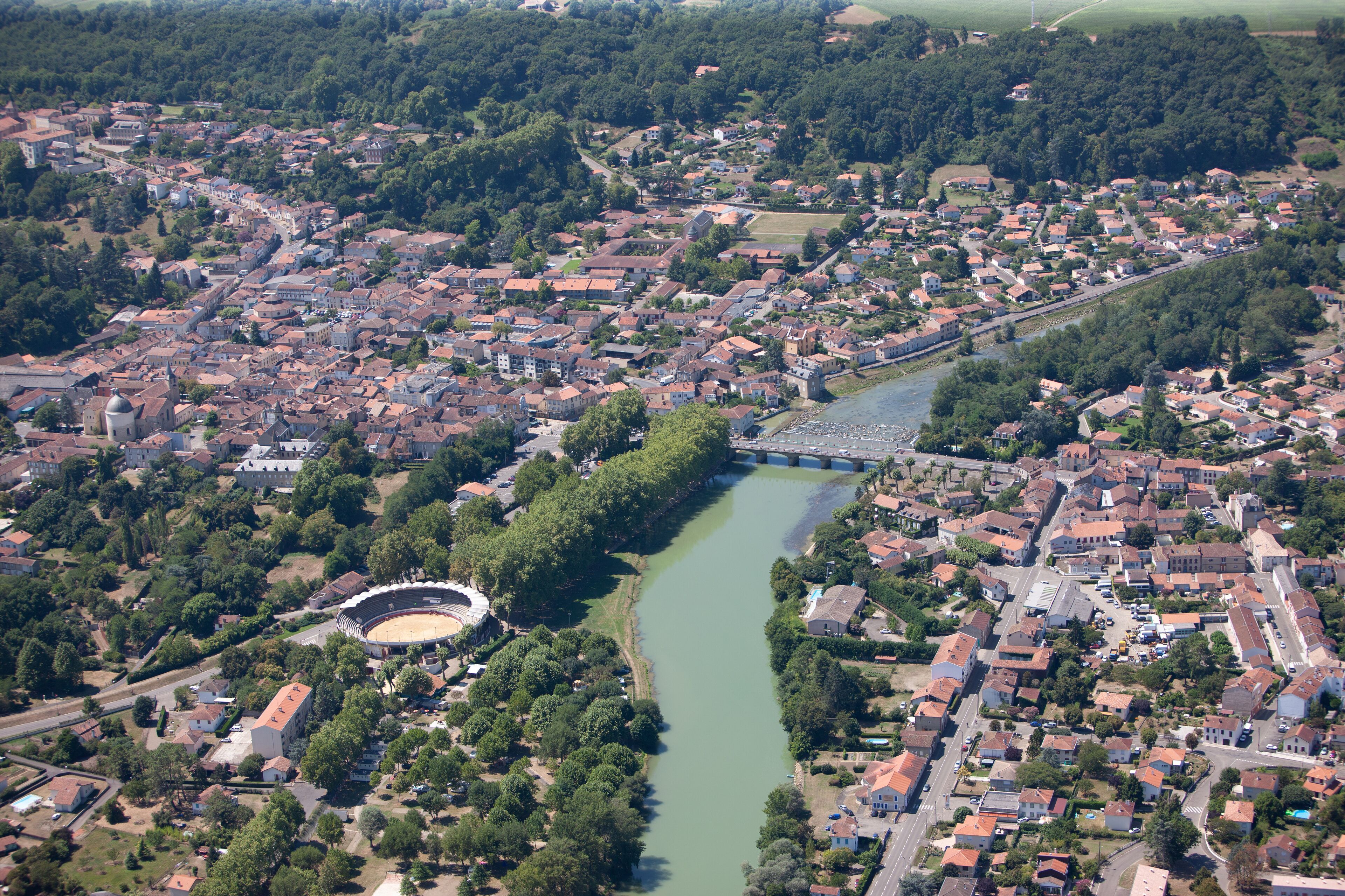 An aerial view of a town with a river, a stadium, and surrounding greenery.