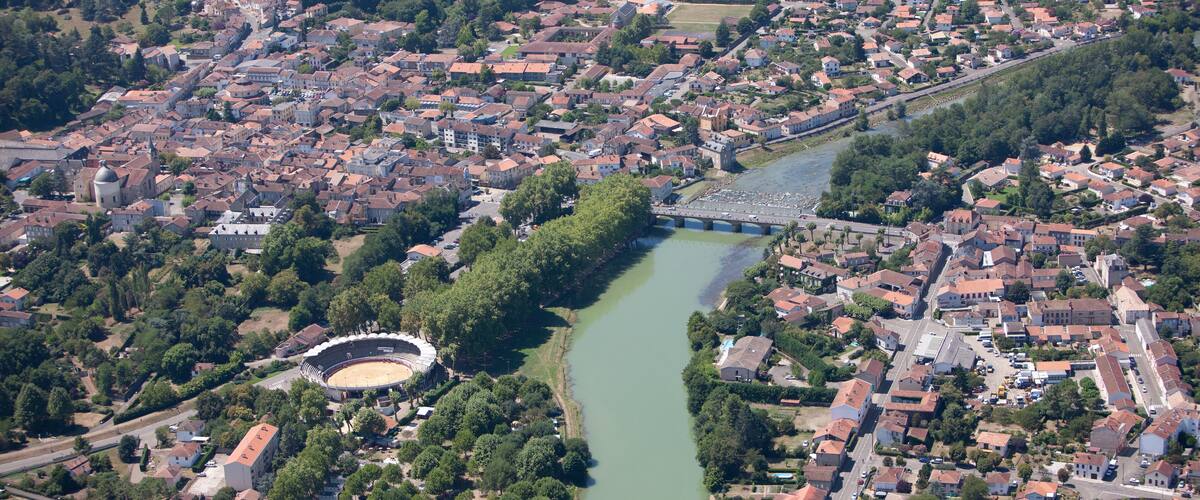 An aerial view of a town with a river, a stadium, and surrounding greenery.