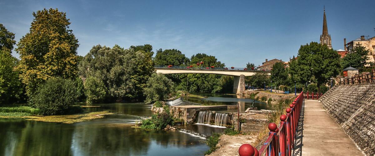 A river with a bridge, a church spire, and a stone wall.