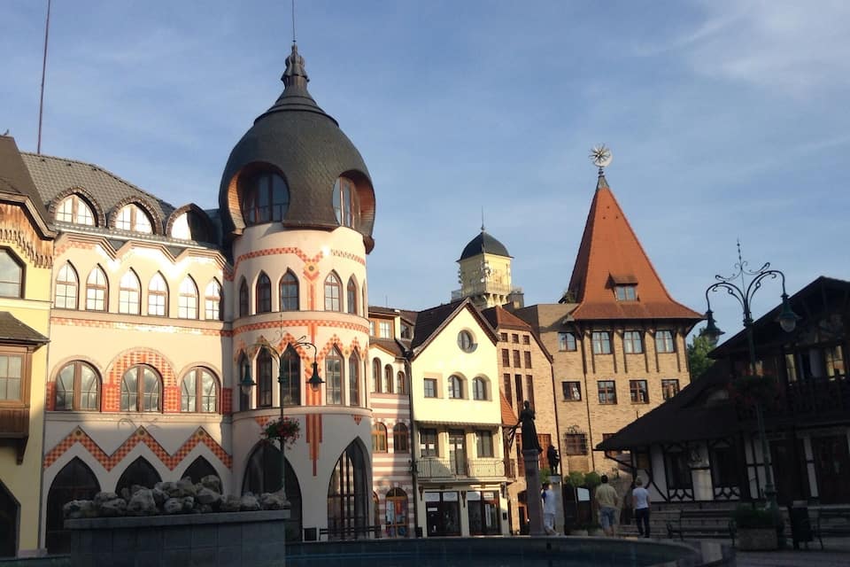 A historic European town square with ornate buildings, a fountain, and a church with a clock tower.