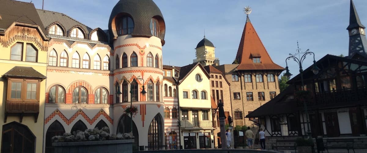 A historic European town square with ornate buildings, a fountain, and a church with a clock tower.