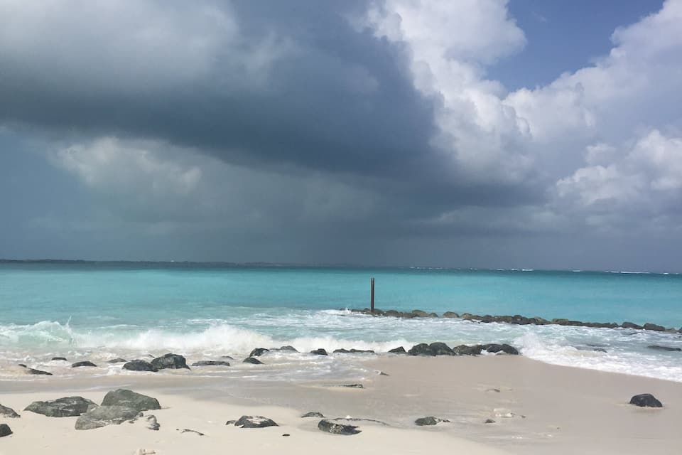 En strand med turkosblått vatten, vit sand och här och var några stenar.