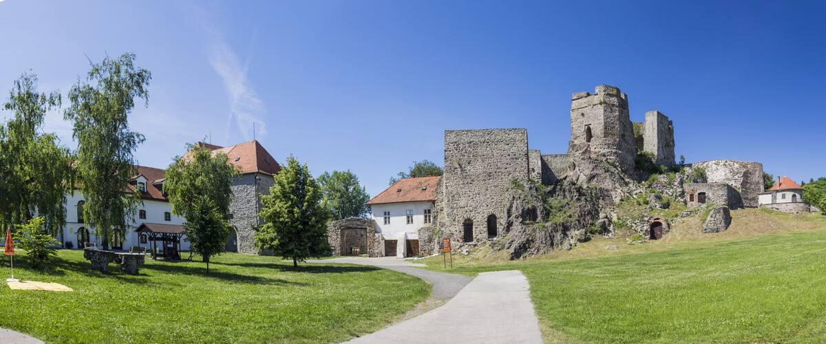 A historic stone castle with a tower, surrounded by lush green grass and a white building with a red roof.