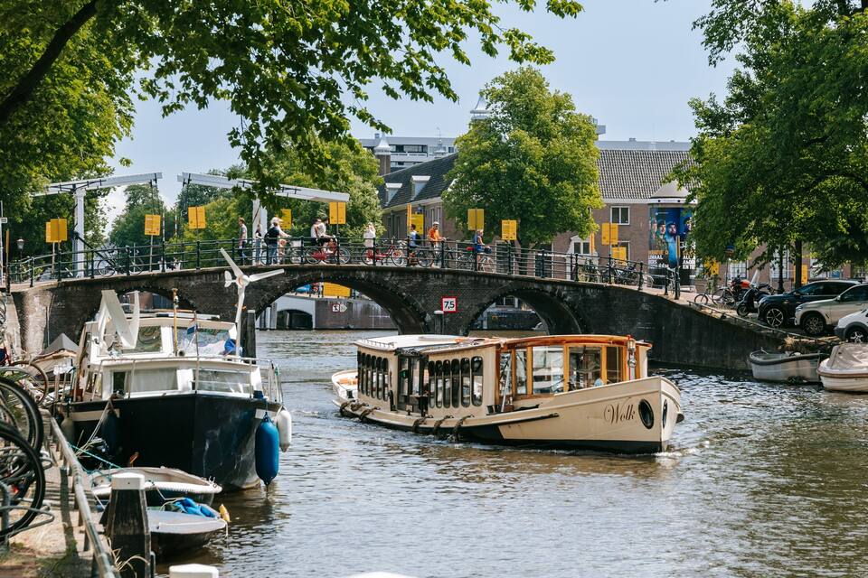 A canal with boats, a bridge, and a cityscape with trees and buildings.