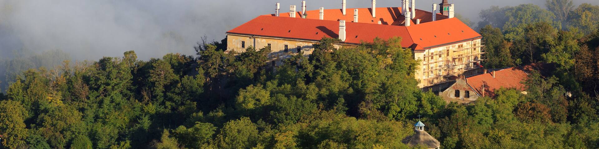 A historic building with a red roof surrounded by dense forest and misty clouds.