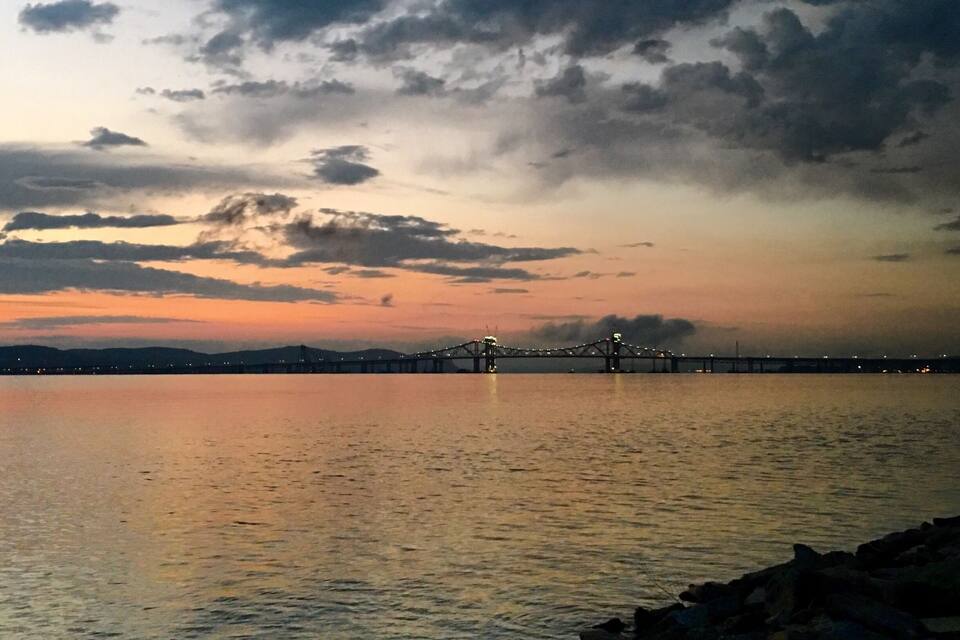 Um pôr do sol sobre águas calmas, com uma ponte ao longe.