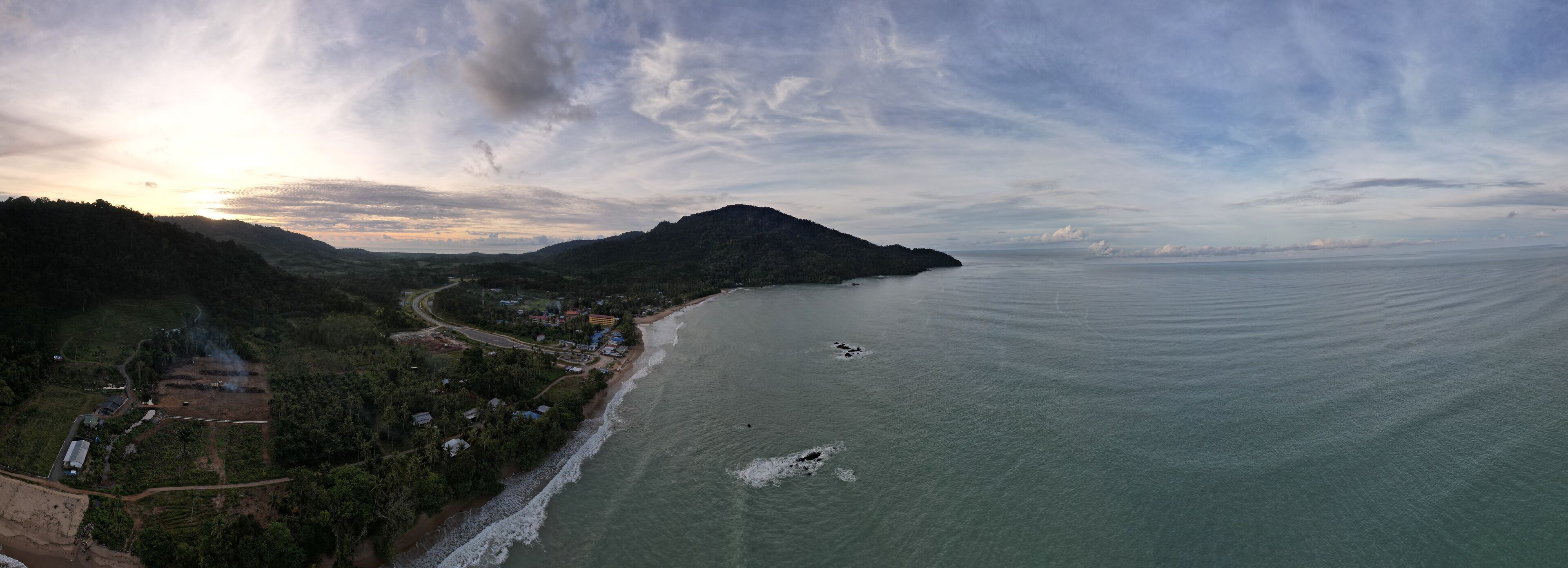 A coastal landscape with a beach, a winding road, and a mountain in the background.