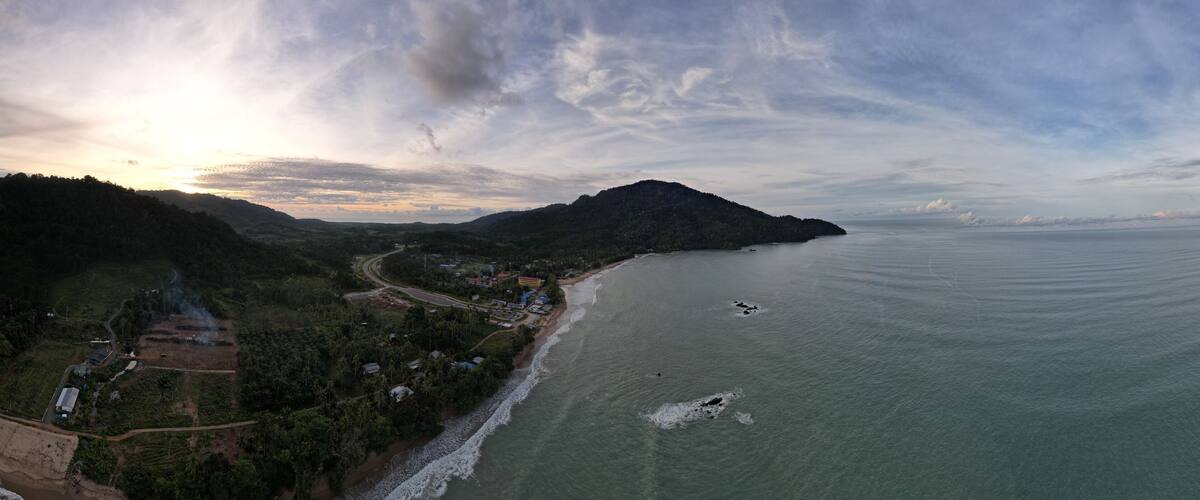 A coastal landscape with a beach, a winding road, and a mountain in the background.