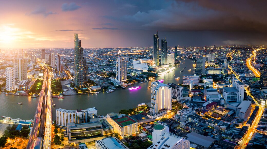 A cityscape with a river, high-rise buildings, and a bridge at sunset.