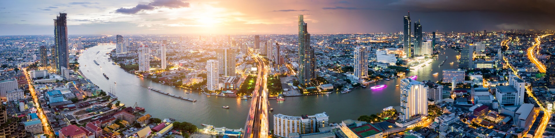 A cityscape with a river, high-rise buildings, and a bridge at sunset.