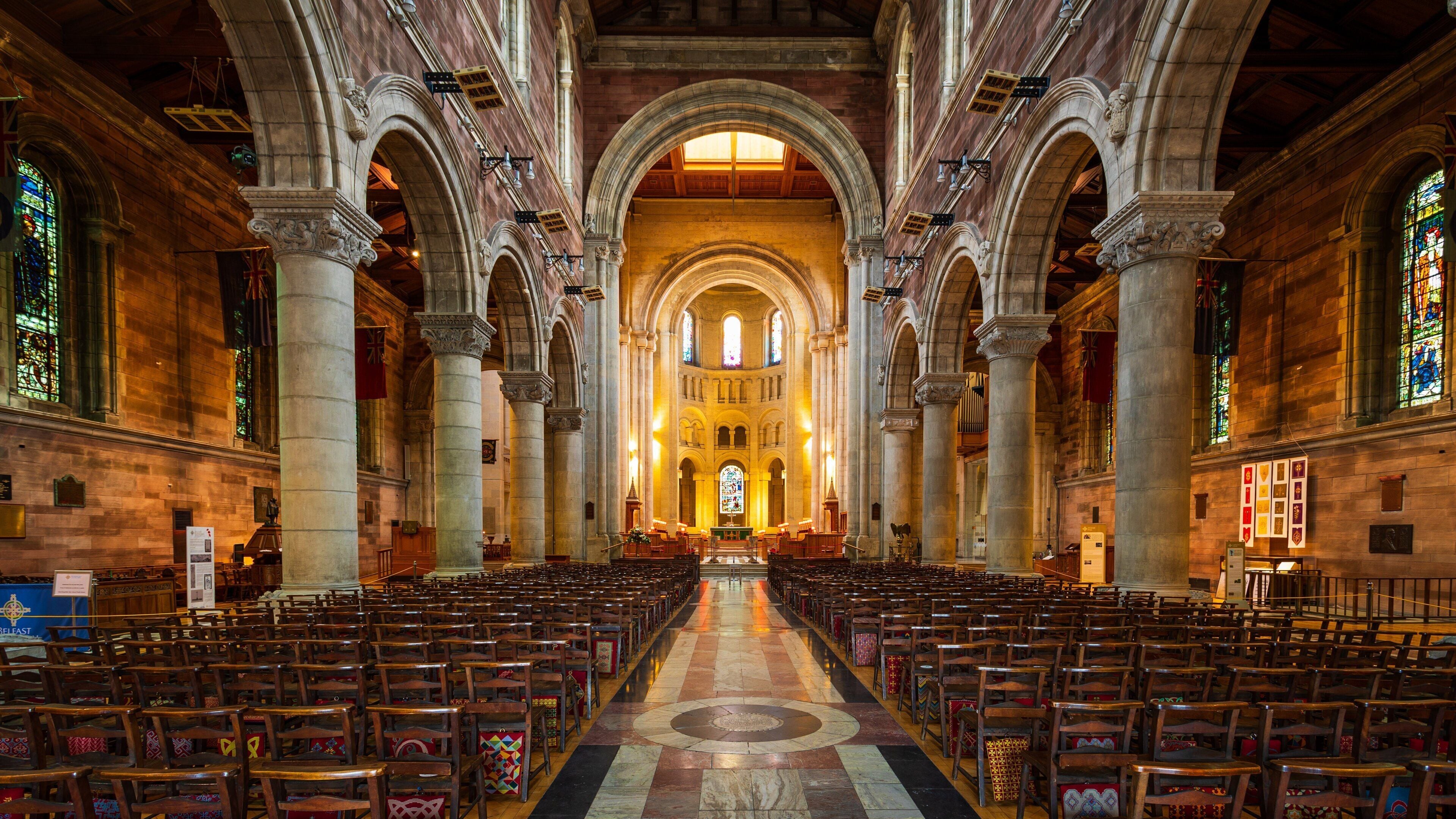 Ein Kircheninneres mit gewölbten Decken, Buntglasfenstern und Reihen hölzerner Kirchenbänke.