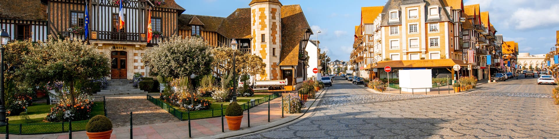 A cobblestone street with historic buildings, a tower, and a clear blue sky.