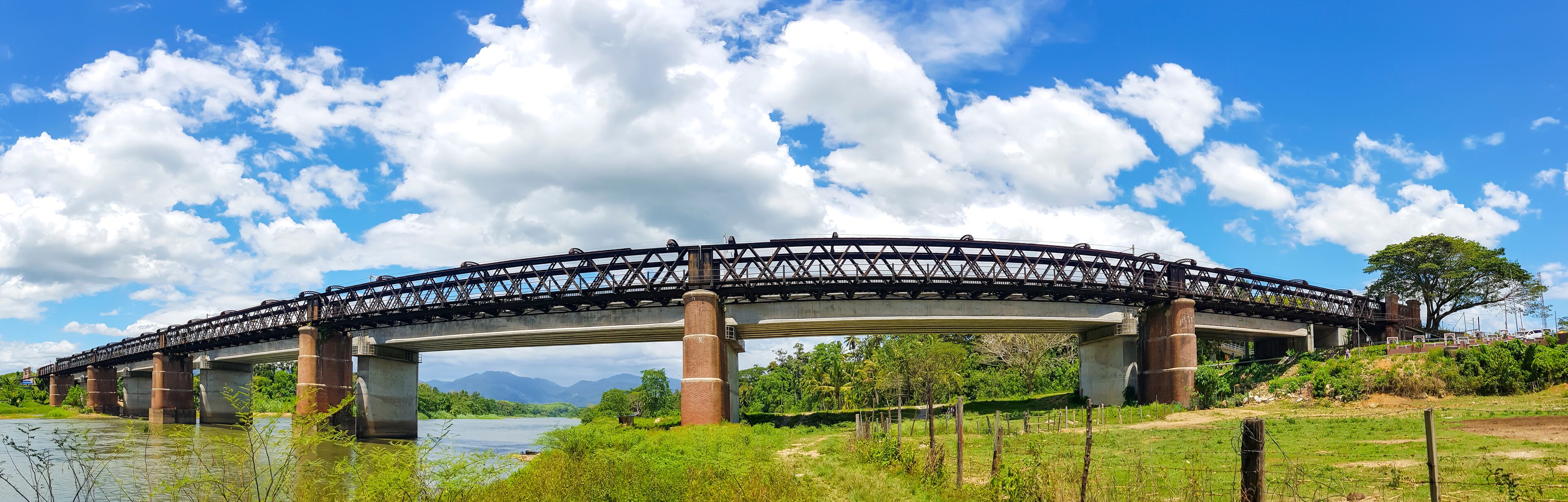 A steel bridge over a river with mountains in the background and a clear sky.
