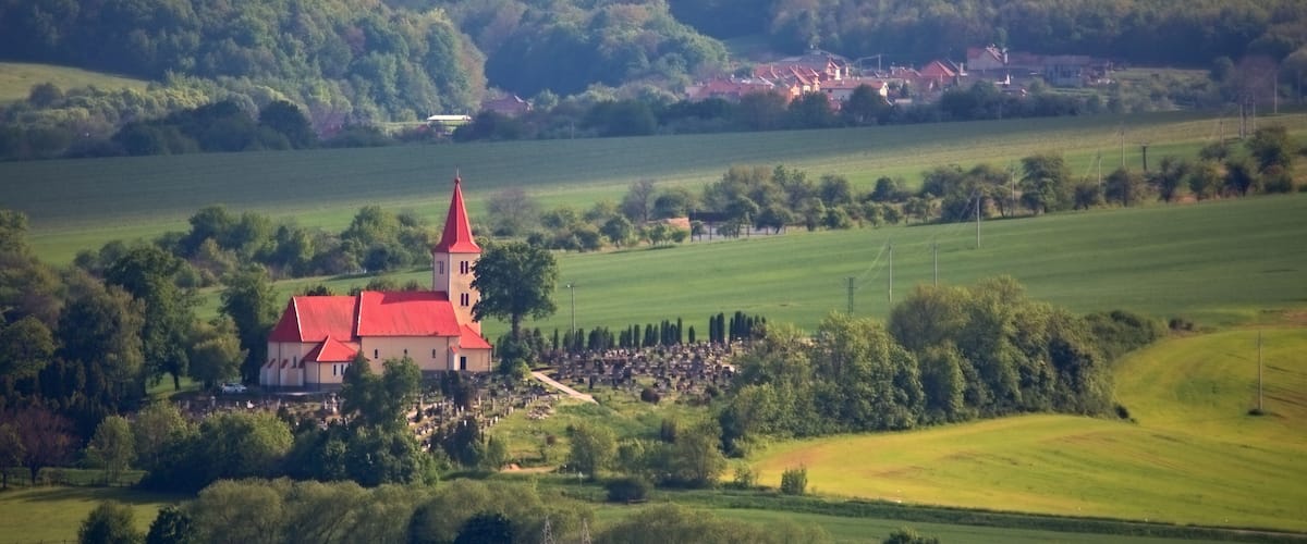 A church with a red roof surrounded by green fields and trees.