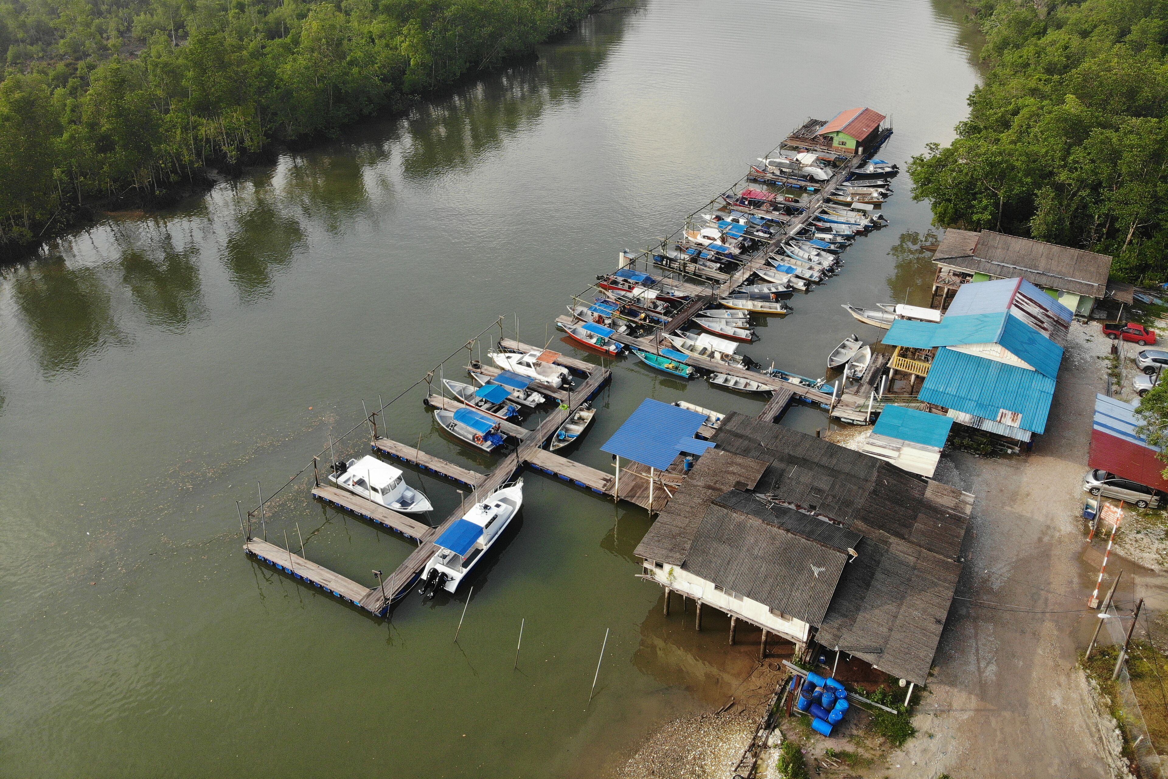 A riverfront with a dock filled with boats and a small building with a blue roof.